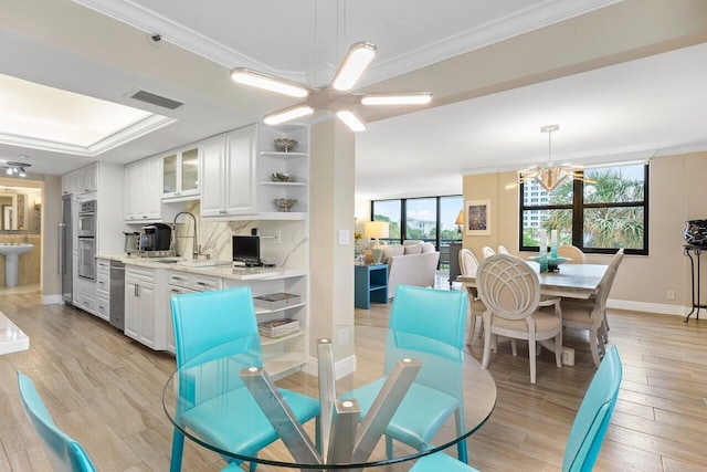 dining area with sink, light hardwood / wood-style flooring, ceiling fan with notable chandelier, and ornamental molding