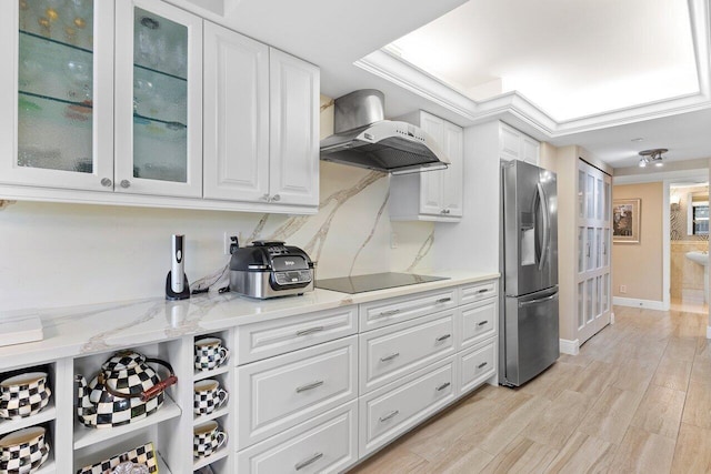 kitchen with black electric cooktop, light hardwood / wood-style flooring, wall chimney exhaust hood, light stone counters, and stainless steel fridge with ice dispenser