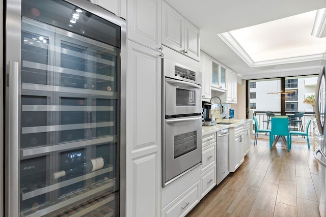 kitchen with a tray ceiling, white cabinets, light hardwood / wood-style floors, wine cooler, and stainless steel appliances