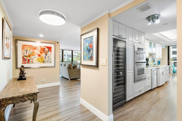 interior space featuring sink, ornamental molding, appliances with stainless steel finishes, light hardwood / wood-style floors, and white cabinets