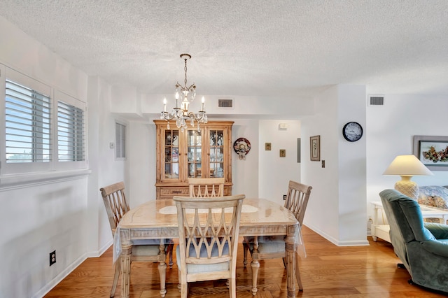 dining area with a chandelier, a textured ceiling, and light hardwood / wood-style floors