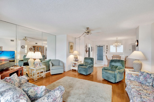 living room with ceiling fan with notable chandelier, wood-type flooring, and a textured ceiling