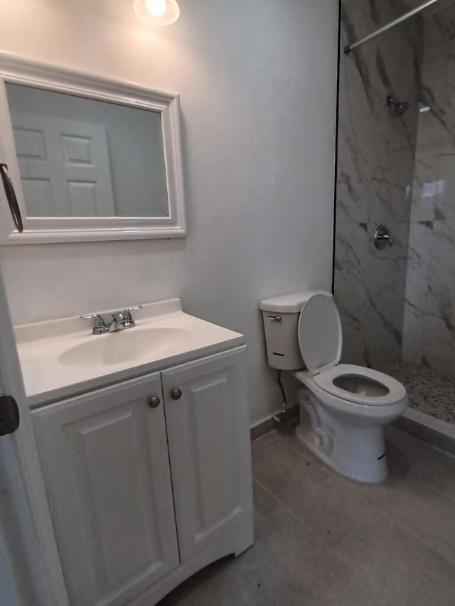 bathroom featuring toilet, vanity, tiled shower, and tile flooring