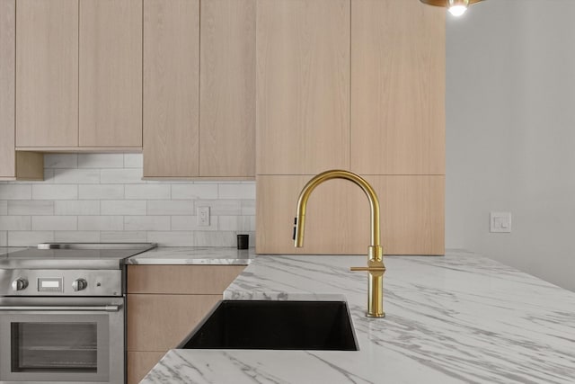 kitchen with light stone counters, light brown cabinets, stainless steel electric stove, and sink