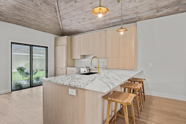 kitchen with light brown cabinetry, light hardwood / wood-style flooring, decorative light fixtures, light stone counters, and kitchen peninsula