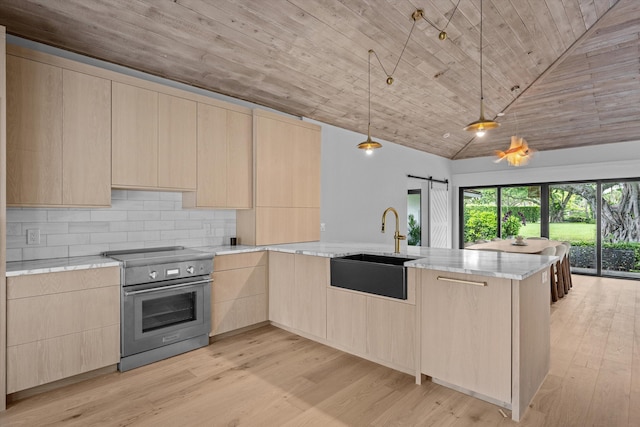 kitchen featuring light brown cabinetry, kitchen peninsula, sink, stainless steel range with electric stovetop, and a barn door