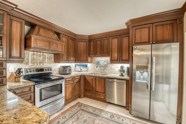 kitchen featuring custom range hood, light stone counters, stainless steel appliances, sink, and a textured ceiling