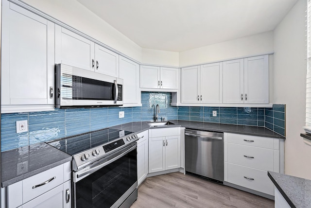 kitchen featuring appliances with stainless steel finishes, tasteful backsplash, sink, white cabinetry, and light hardwood / wood-style flooring