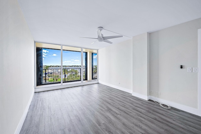 spare room featuring ceiling fan, a wall of windows, and dark wood-type flooring