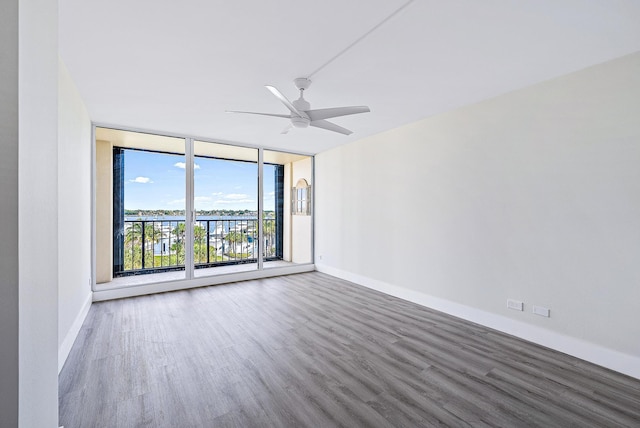 unfurnished room featuring dark hardwood / wood-style flooring, ceiling fan, and a wall of windows