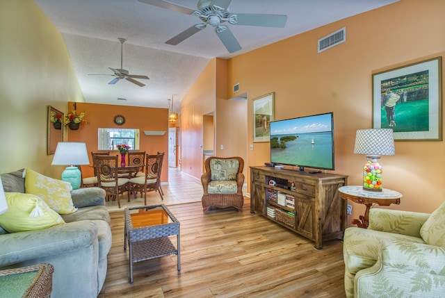 living room with a textured ceiling, vaulted ceiling, ceiling fan, and light wood-type flooring