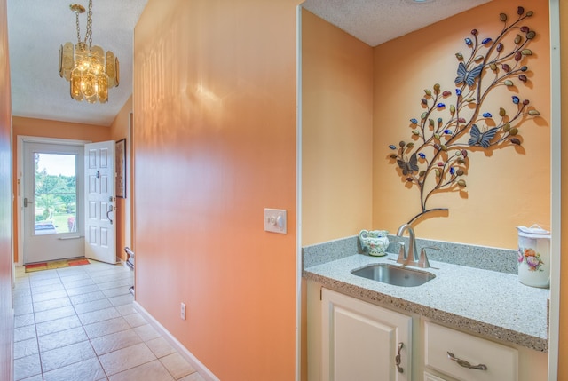 interior space featuring light tile flooring, light stone countertops, a textured ceiling, sink, and an inviting chandelier