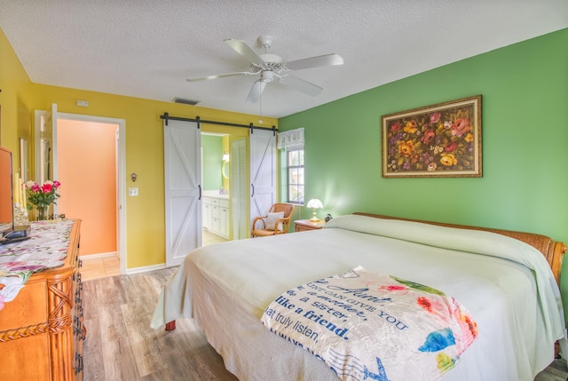 bedroom with hardwood / wood-style floors, ceiling fan, a barn door, a textured ceiling, and ensuite bath