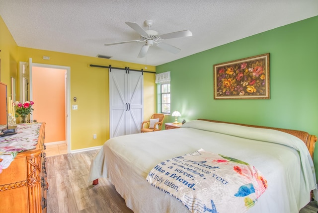 bedroom with a barn door, hardwood / wood-style floors, a textured ceiling, and ceiling fan