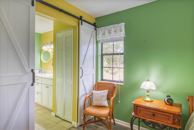 sitting room featuring a barn door, light tile floors, and a textured ceiling