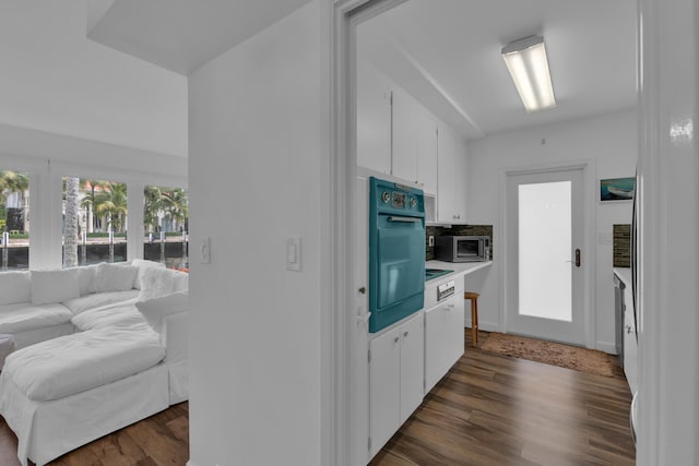 kitchen with backsplash, black oven, white cabinetry, and dark hardwood / wood-style flooring