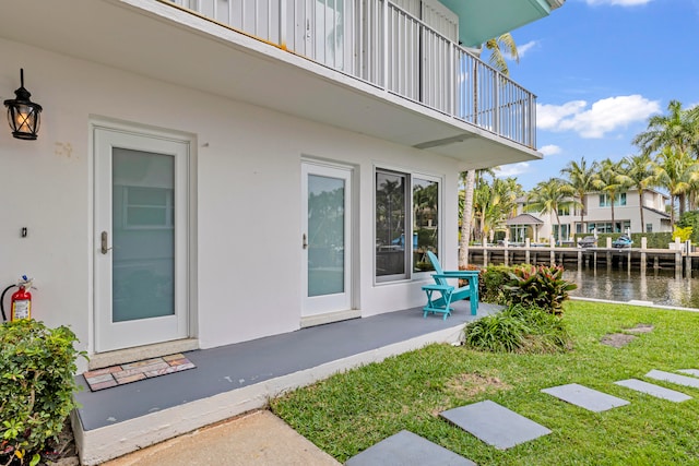 property entrance with a balcony, a water view, a yard, and a patio area