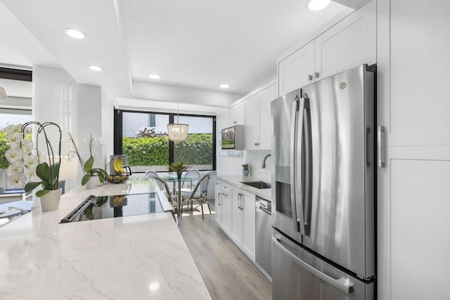 kitchen with light stone countertops, stainless steel appliances, light wood-type flooring, and white cabinetry