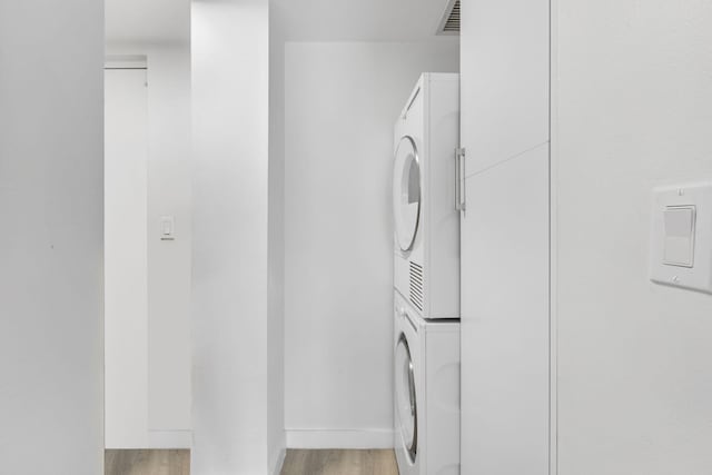 clothes washing area featuring light hardwood / wood-style floors and stacked washing maching and dryer