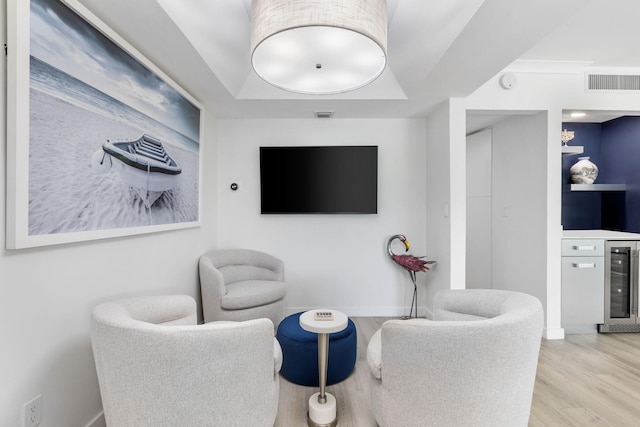 sitting room featuring light hardwood / wood-style flooring, beverage cooler, and a raised ceiling