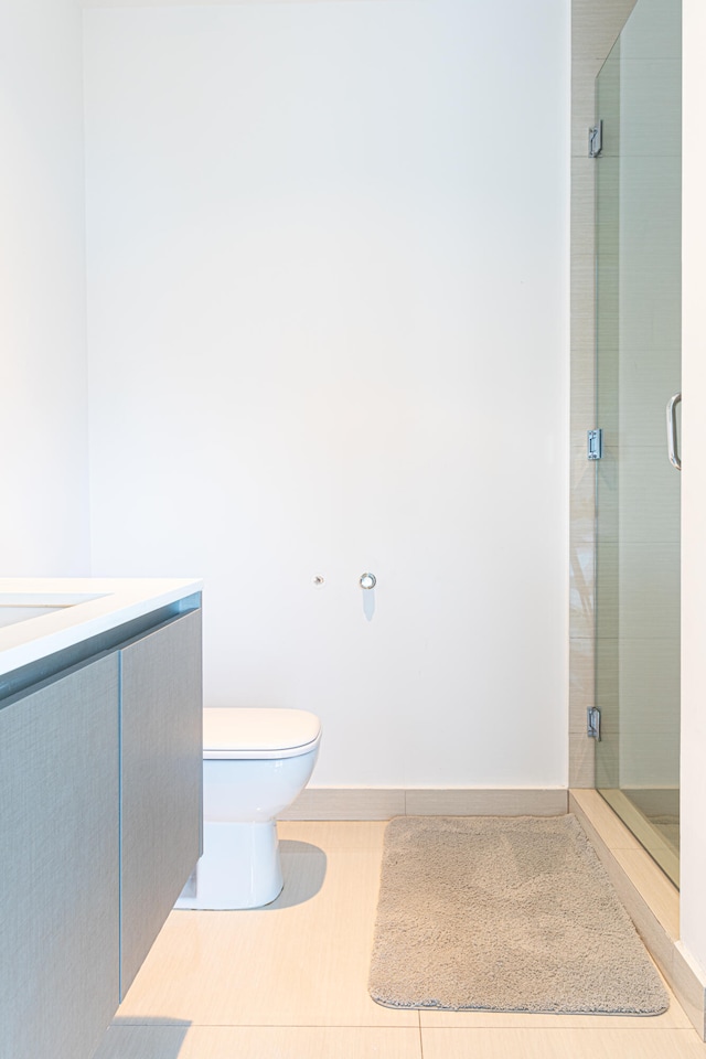 bathroom featuring a shower with shower door, tile patterned flooring, toilet, and vanity