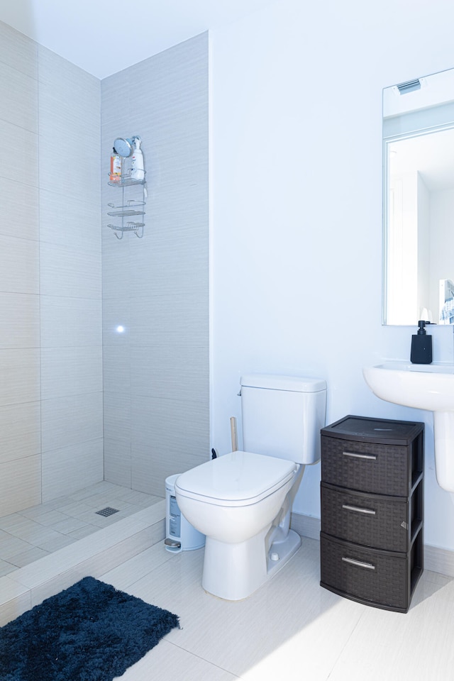 bathroom with toilet, tiled shower, and tile patterned floors