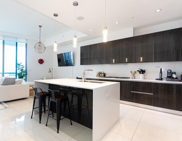 kitchen featuring a breakfast bar area, pendant lighting, light tile patterned floors, an island with sink, and sink