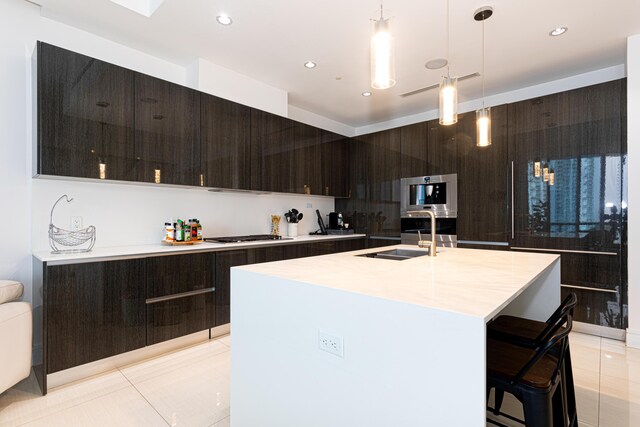 kitchen featuring a kitchen bar, decorative light fixtures, light tile patterned floors, sink, and a center island with sink