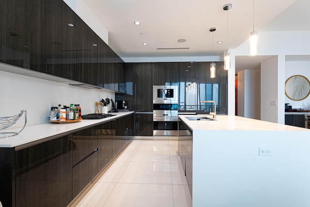 kitchen featuring hanging light fixtures, light tile patterned floors, stainless steel appliances, sink, and a center island with sink