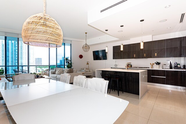 kitchen featuring dark brown cabinets, floor to ceiling windows, a center island with sink, and hanging light fixtures