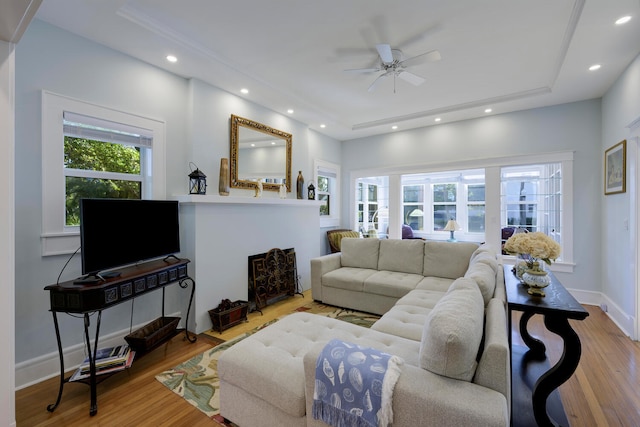 living room with light wood-type flooring, ceiling fan, and a raised ceiling