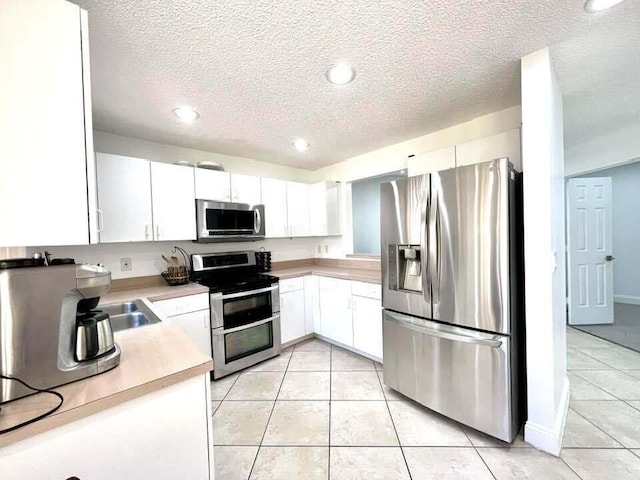 kitchen featuring white cabinetry, appliances with stainless steel finishes, sink, light tile floors, and a textured ceiling