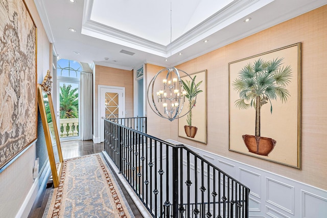 hall with a tray ceiling, crown molding, wood-type flooring, and an inviting chandelier