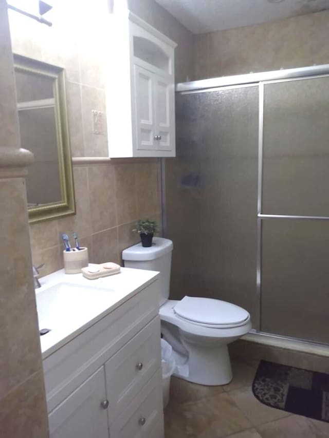 bathroom with toilet, tile walls, vanity with extensive cabinet space, backsplash, and tile floors