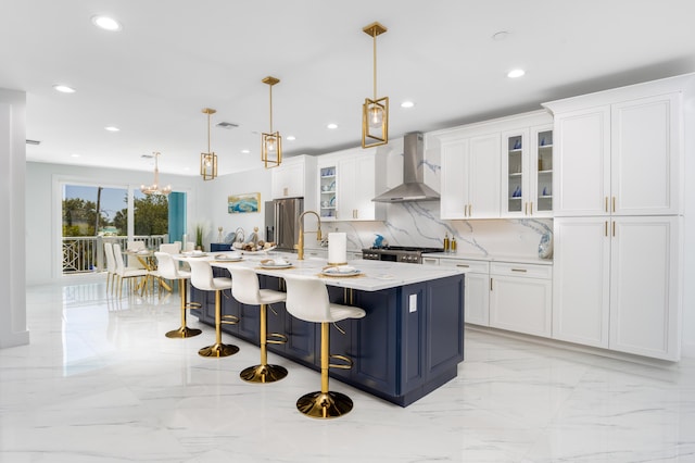 kitchen featuring a center island with sink, white cabinets, pendant lighting, and wall chimney range hood