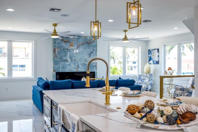 kitchen featuring decorative light fixtures, light stone countertops, a wealth of natural light, and sink