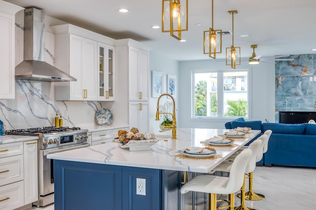 kitchen with wall chimney range hood, white cabinetry, a center island with sink, and gas range