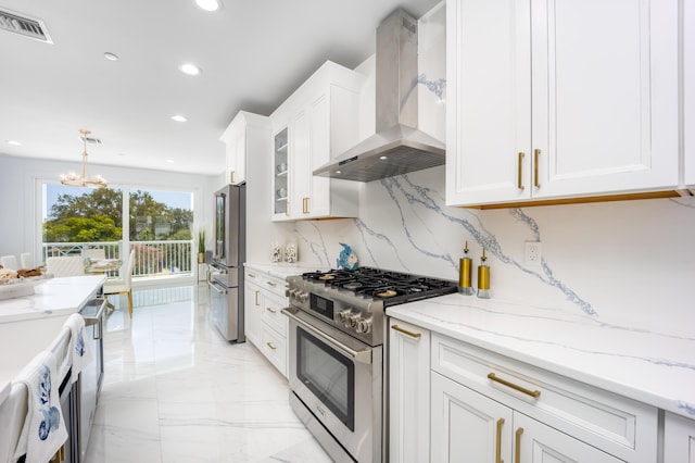 kitchen featuring premium appliances, white cabinets, wall chimney exhaust hood, hanging light fixtures, and a notable chandelier