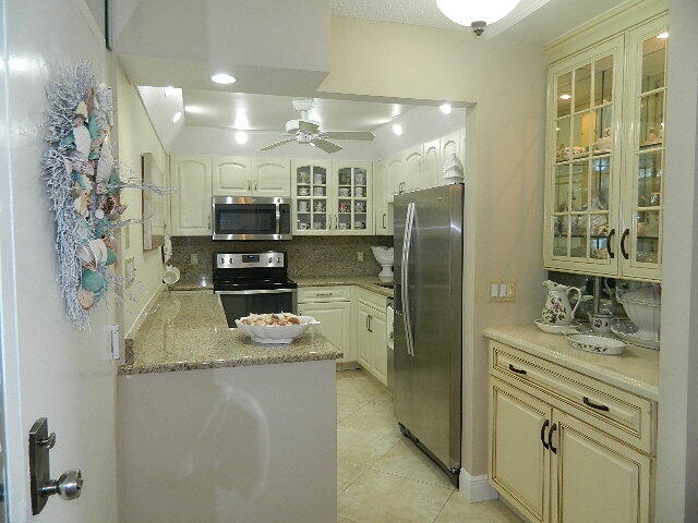 kitchen featuring light tile patterned floors, a ceiling fan, appliances with stainless steel finishes, decorative backsplash, and glass insert cabinets