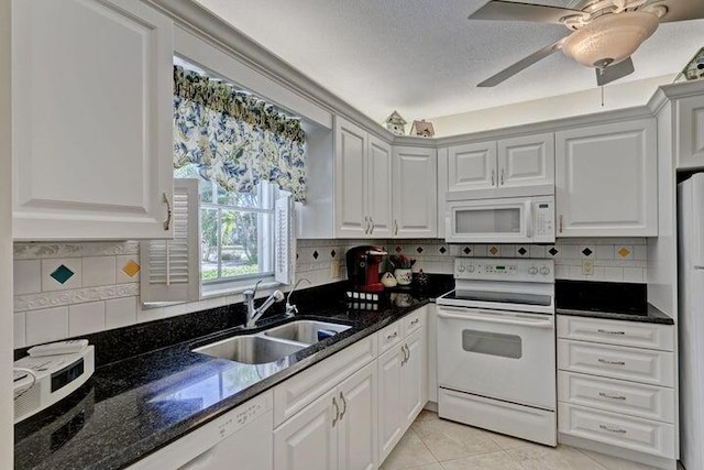 kitchen with white appliances, white cabinetry, light tile patterned floors, sink, and dark stone countertops