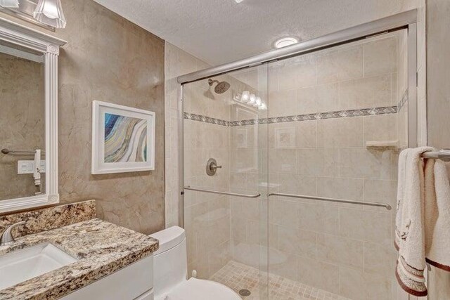 bathroom featuring vanity, toilet, walk in shower, and a textured ceiling