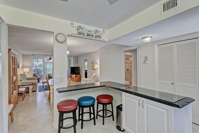 kitchen featuring kitchen peninsula, white cabinetry, light tile patterned flooring, a textured ceiling, and a breakfast bar