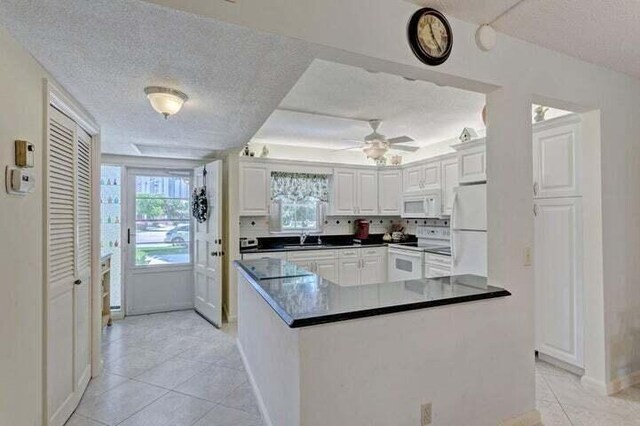 kitchen featuring white appliances, white cabinets, sink, kitchen peninsula, and light tile patterned floors