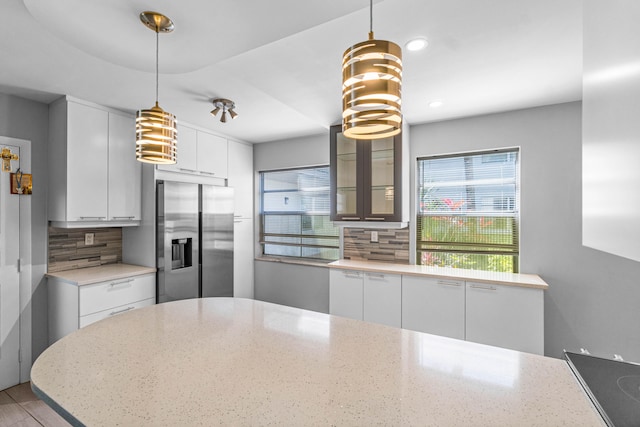 kitchen featuring light stone counters, stainless steel fridge with ice dispenser, hanging light fixtures, tasteful backsplash, and white cabinetry