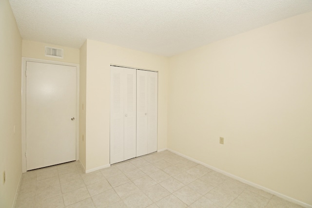 unfurnished bedroom featuring light tile floors, a textured ceiling, and a closet