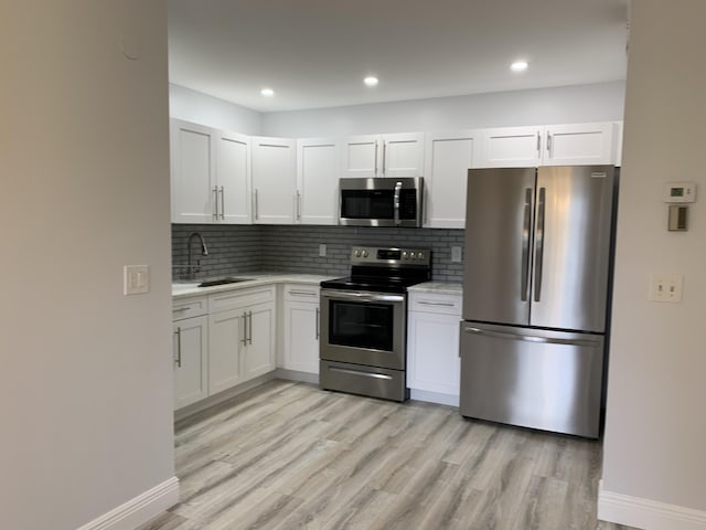 kitchen featuring white cabinets, sink, tasteful backsplash, light hardwood / wood-style floors, and stainless steel appliances