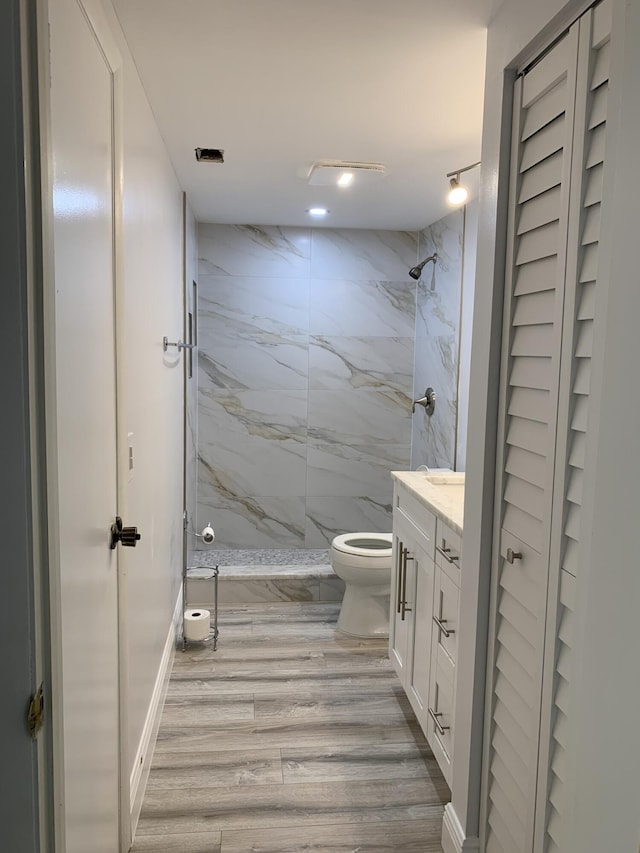 bathroom with toilet, vanity, wood-type flooring, and tiled shower