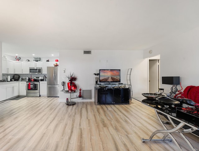 kitchen with decorative backsplash, white cabinets, stainless steel appliances, and light hardwood / wood-style floors