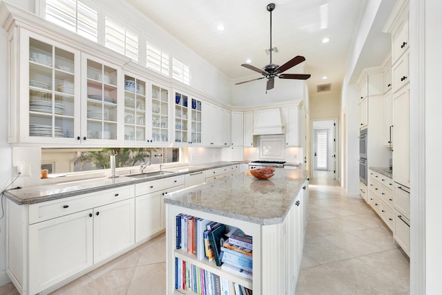 kitchen featuring white cabinetry, a kitchen island, light stone counters, light tile patterned flooring, and custom exhaust hood