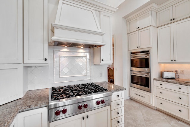 kitchen with light stone countertops, light tile flooring, appliances with stainless steel finishes, custom exhaust hood, and tasteful backsplash